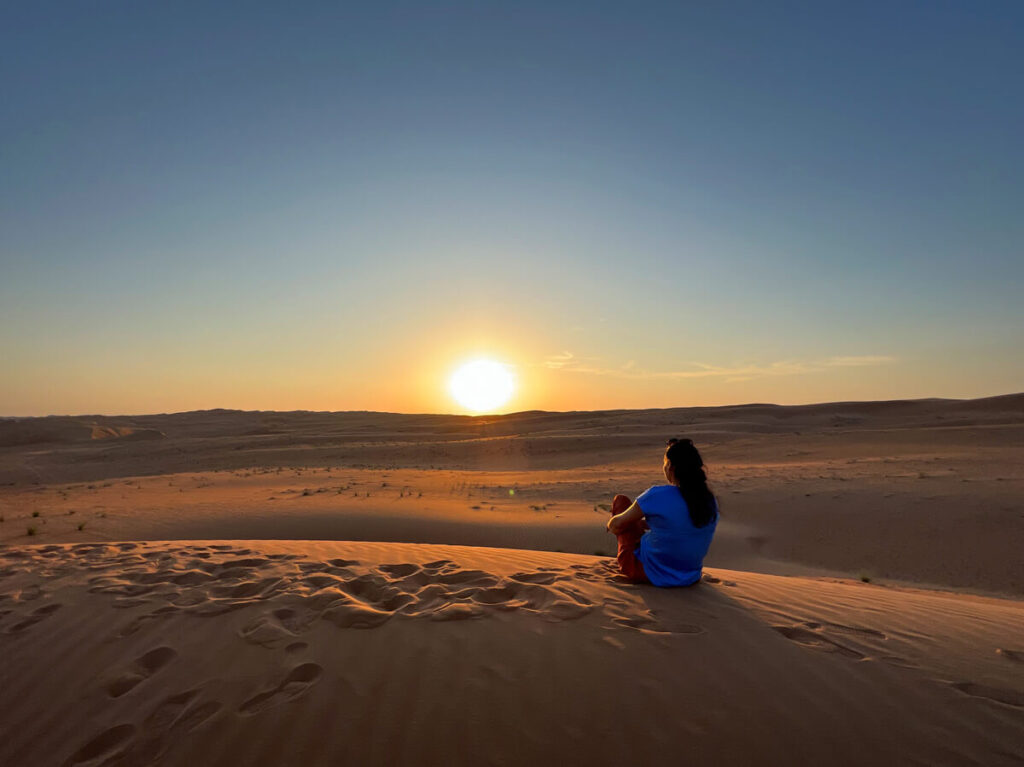 Sonnenuntergang mit Frau in der Wüste Wahiba Sands im Oman