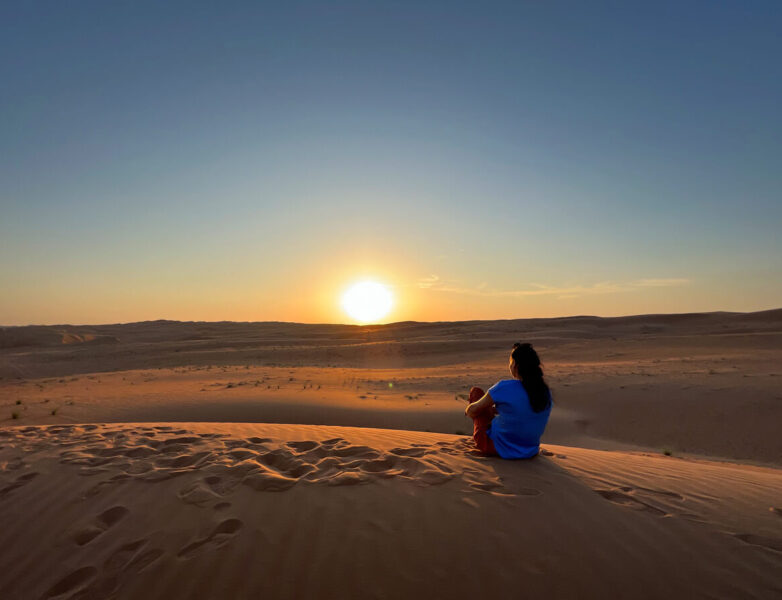 Sonnenuntergang mit Frau in der Wüste Wahiba Sands im Oman