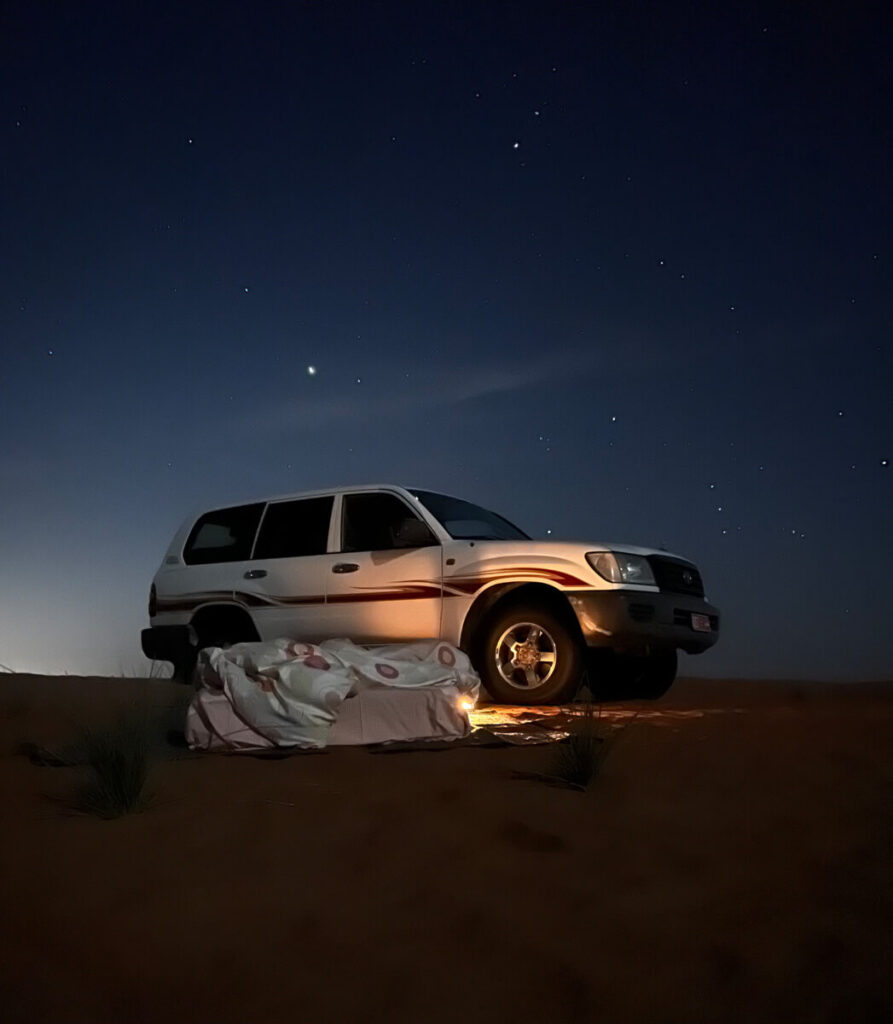 Auto und Bett unter dem Sternenhimmel in der Wüste im Oman