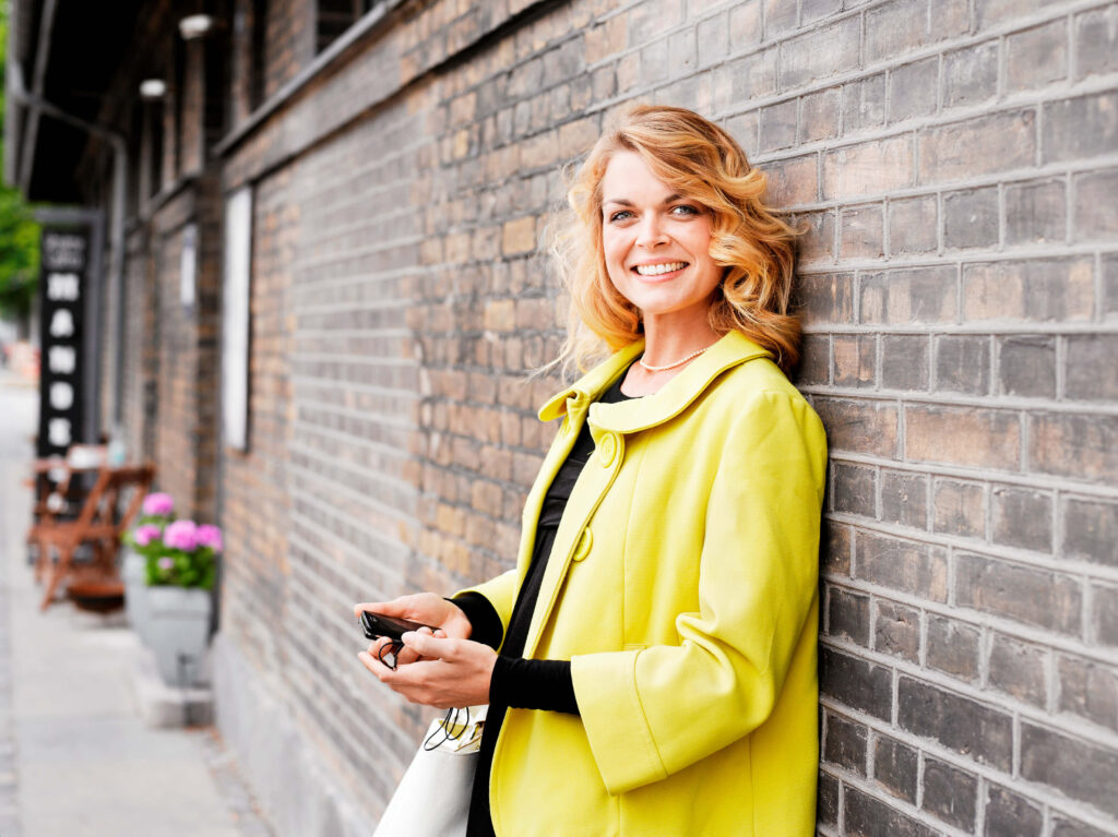 Frau mit gelber Jacke an einer Mauer